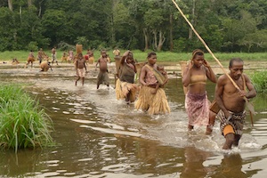 “Larry Whitman” (Kris Marshall) and the pygmies crossing the water in a scene from OKA!